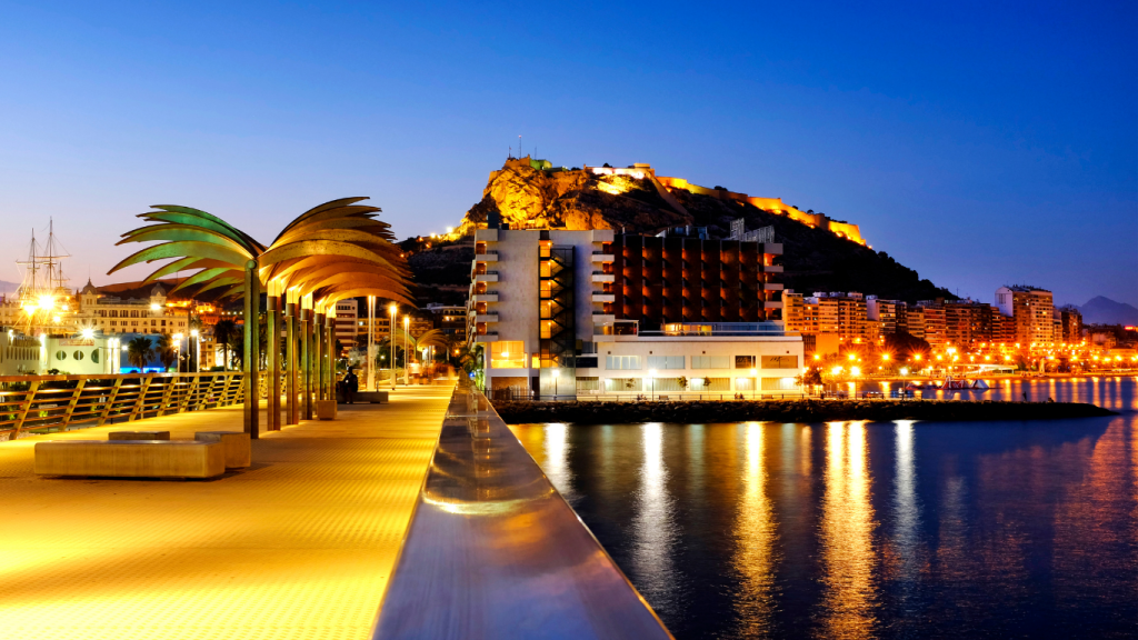 Escena de la noche de San Juan en Alicante con hogueras, playa y personas celebrando, representando la oportunidad de conectar con clientes desde el marketing local